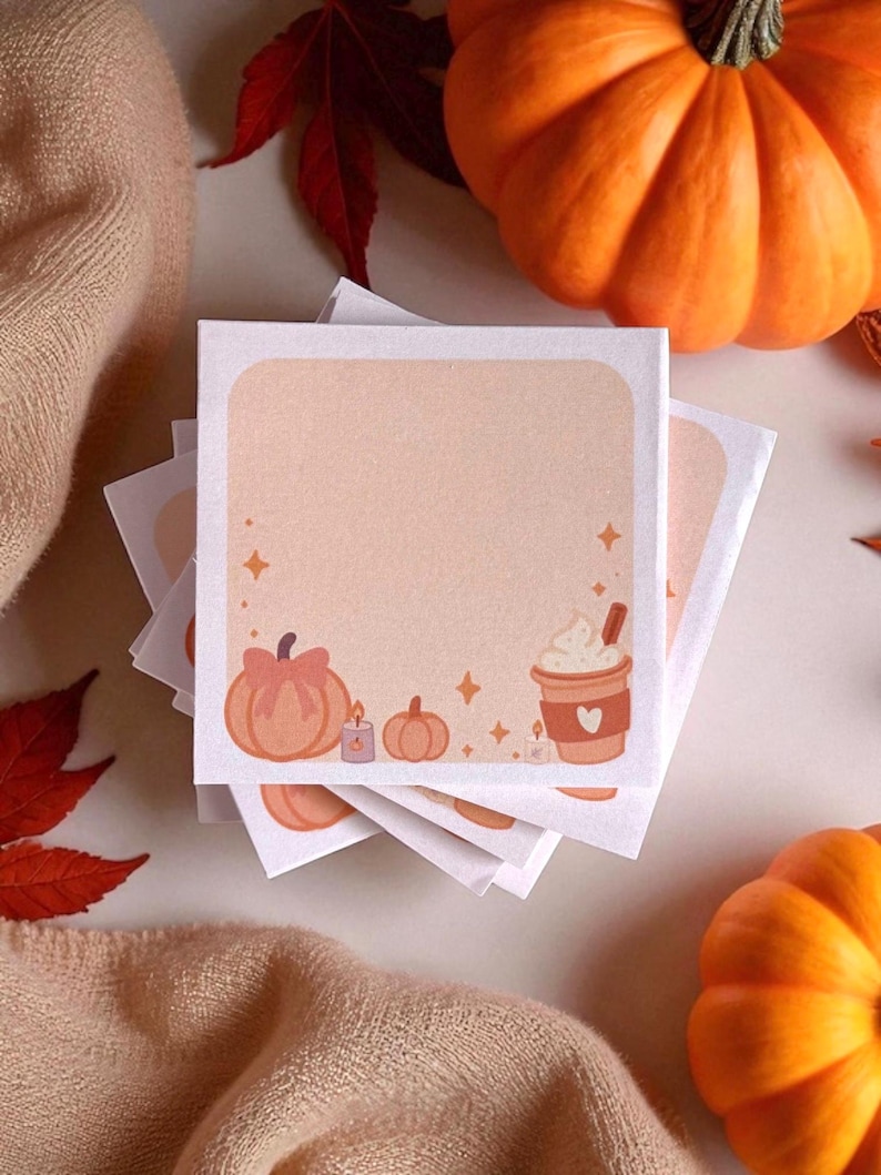 Pu&ograve; includere: Una pila di foglietti adesivi quadrati con uno sfondo color pesca chiaro e un bordo bianco. Il bordo inferiore presenta illustrazioni di una zucca con un fiocco, una piccola candela, una zucca pi&ugrave; piccola e una tazza di caff&egrave; con panna.