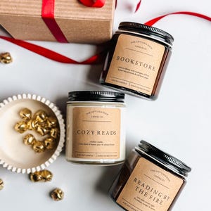 May include: Three soy candles in glass jars with black lids. The candles are labeled "Bookstore", "Cozy Reads", and "Reading by the Fire". Each candle has a brown label with white text and is hand-poured in Texas.