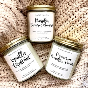 May include: Three 8-ounce soy wax candles in glass jars with gold lids. The candles are labeled "Pumpkin Caramel Dreams", "Cinnamon Pumpkin Cream", and "Vanilla Chestnut". Each label includes fragrance notes and the text "hand-poured in small batches".