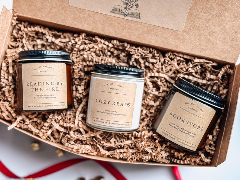 May include: Three candles in a brown box with shredded paper. The candles are labeled "Reading by the Fire", "Cozy Reads", and "Bookstore".