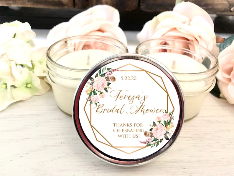 Pode incluir: Uma vela branca em um frasco de vidro transparente com um r&oacute;tulo com padr&atilde;o floral dourado que diz "Teresa's Bridal Shower 5.22.20 Thanks for celebrating with us!"