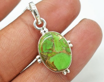 Puede incluir: Un colgante de plata con una piedra ovalada de turquesa verde y marrón. El colgante está engastado en un marco de plata con pequeñas cuentas de plata alrededor del borde.