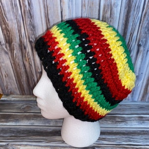 May include: A crocheted beanie hat with black, red, yellow, and green stripes. The hat is on a white mannequin head.