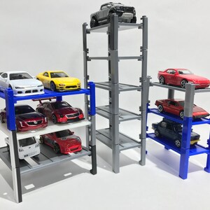 Peut inclure: Un garage &agrave; voitures miniature &agrave; plusieurs niveaux avec quatre &eacute;tages. Le garage est en plastique gris et a des supports bleus. Il y a huit voitures miniatures gar&eacute;es sur le garage, dont une voiture rouge, une voiture blanche, une voiture jaune, une voiture bleue et un camion gris.