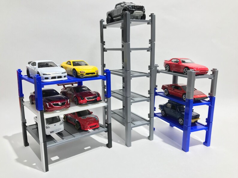 Peut inclure: Un garage &agrave; voitures miniature &agrave; plusieurs niveaux avec quatre &eacute;tages. Le garage est en plastique gris et a des supports bleus. Il y a huit voitures miniatures gar&eacute;es sur le garage, dont une voiture rouge, une voiture blanche, une voiture jaune, une voiture bleue et un camion gris.