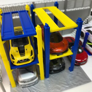 Peut inclure: Un garage de stationnement pour voitures miniatures jaune, bleu et blanc &agrave; quatre niveaux. Le garage est dot&eacute; de supports jaunes et bleus et de plateformes jaunes et bleues. Cinq voitures miniatures sont gar&eacute;es sur les plateformes, dont une jaune, une rouge, une blanche, une grise et une rouge.