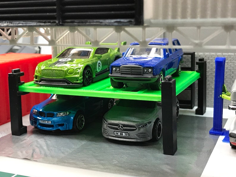 Peut inclure: Un garage de stationnement pour voitures miniatures vert, bleu et argent avec quatre voitures miniatures gar&eacute;es &agrave; l'int&eacute;rieur. Les voitures sont une Bentley verte, une Mercedes-Benz bleue, une BMW bleue et une Mercedes-Benz argent&eacute;e.