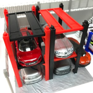 Peut inclure: Un garage de stationnement pour voitures miniatures rouge, noir et argent avec quatre niveaux. Le garage est en plastique et poss&egrave;de un cadre en m&eacute;tal noir. Quatre voitures miniatures sont gar&eacute;es dans le garage, dont une voiture de sport rouge, une voiture de sport argent&eacute;e, une berline argent&eacute;e et une voiture de sport orange.