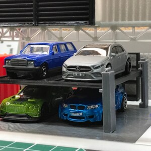 Peut inclure: Un garage &agrave; voitures &agrave; plusieurs niveaux avec quatre voitures miniatures. Les voitures sont une familiale bleue, une berline argent&eacute;e, une voiture de sport verte et une voiture de sport bleue. Les voitures ont des plaques d'immatriculation qui indiquent "100 MB 20" et "BMW M1".