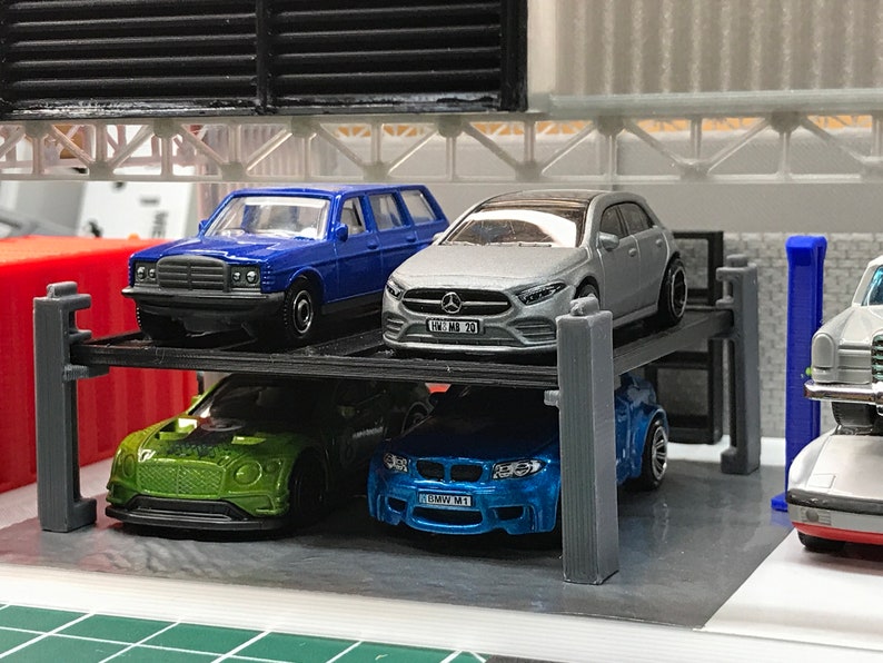 Peut inclure: Un garage &agrave; voitures &agrave; plusieurs niveaux avec quatre voitures miniatures. Les voitures sont une familiale bleue, une berline argent&eacute;e, une voiture de sport verte et une voiture de sport bleue. Les voitures ont des plaques d'immatriculation qui indiquent "100 MB 20" et "BMW M1".