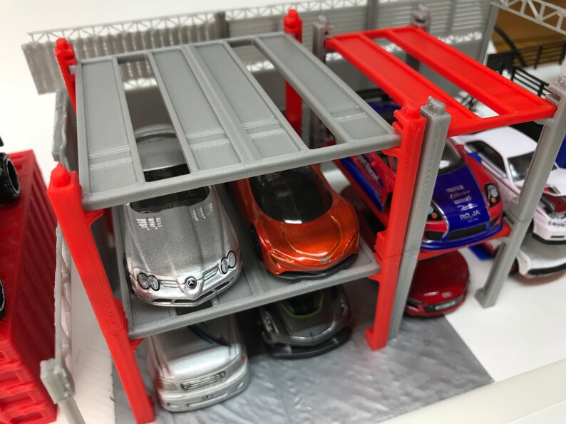 Peut inclure: Un garage &agrave; voitures miniature &agrave; plusieurs niveaux avec des supports en m&eacute;tal gris et rouge. Le garage est rempli de voitures miniatures de diff&eacute;rentes couleurs, notamment argent, rouge, bleu et blanc.