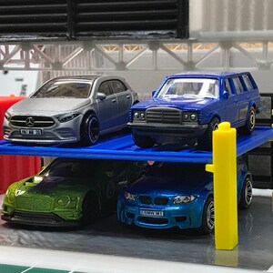 Peut inclure: Un garage de stationnement pour voitures miniatures bleu, jaune et gris avec quatre voitures miniatures gar&eacute;es &agrave; l'int&eacute;rieur. Les voitures sont une Mercedes-Benz argent&eacute;e, une Mercedes-Benz bleue, une Bentley verte et une BMW bleue.