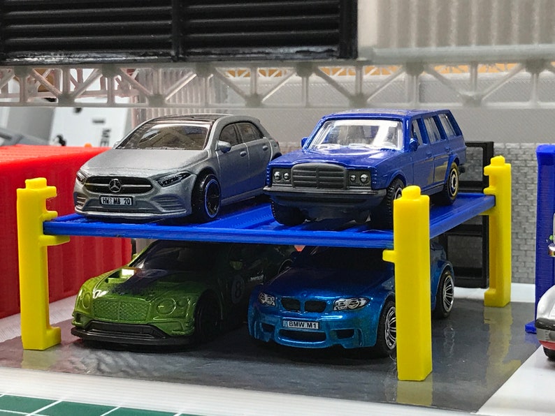 Peut inclure: Un garage de stationnement pour voitures miniatures bleu, jaune et gris avec quatre voitures miniatures gar&eacute;es &agrave; l'int&eacute;rieur. Les voitures sont une Mercedes-Benz argent&eacute;e, une Mercedes-Benz bleue, une Bentley verte et une BMW bleue.