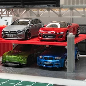 Peut inclure: Un ensemble de garage &agrave; plusieurs niveaux avec quatre voitures miniatures. Les voitures sont une berline argent&eacute;e, une d&eacute;capotable rouge, une voiture de sport verte et un coup&eacute; bleu. Les voitures ont des plaques d'immatriculation qui indiquent "HMF1 RB", "BMW M1" et "ML MB 70".