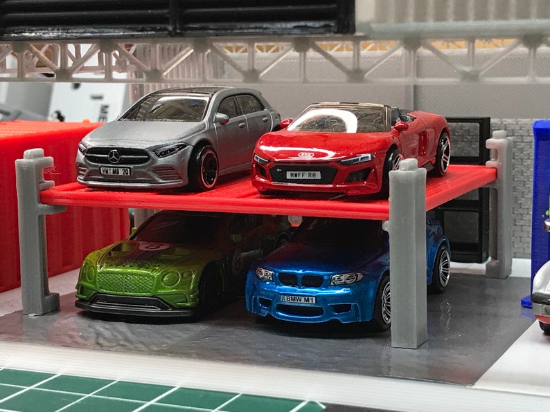 Peut inclure: Un ensemble de garage &agrave; plusieurs niveaux avec quatre voitures miniatures. Les voitures sont une berline argent&eacute;e, une d&eacute;capotable rouge, une voiture de sport verte et un coup&eacute; bleu. Les voitures ont des plaques d'immatriculation qui indiquent "HMF1 RB", "BMW M1" et "ML MB 70".