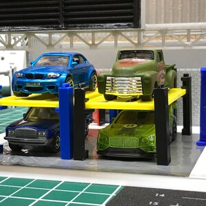 Peut inclure: Un &eacute;l&eacute;vateur de voiture jouet avec quatre voitures dessus. Les voitures sont une BMW M1 bleue, un pick-up vert, une Mercedes-Benz bleue et une Bentley verte.