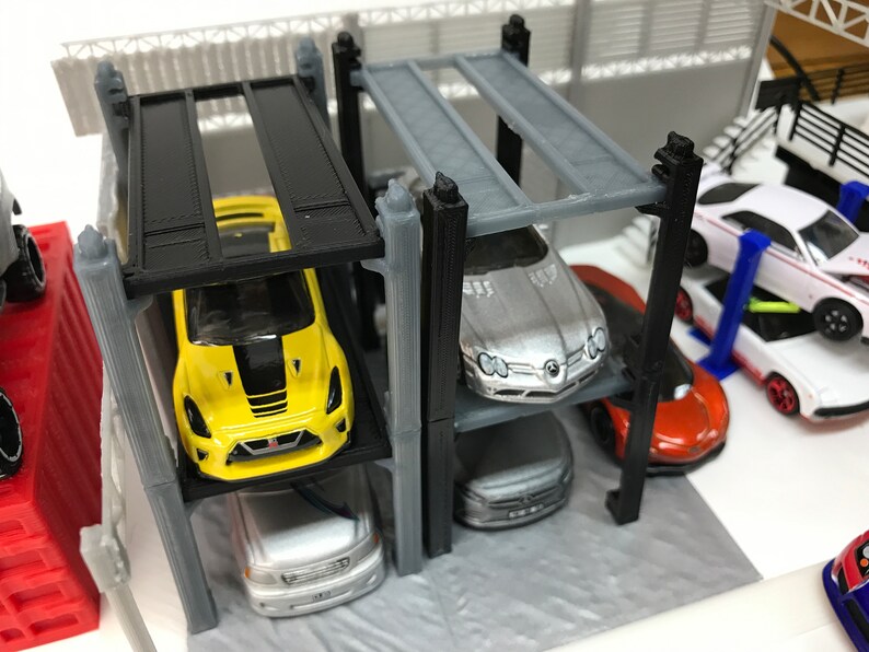 Peut inclure: Un garage &agrave; voitures miniature &agrave; plusieurs niveaux avec quatre voitures miniatures. Le garage est en plastique noir et gris. Les voitures sont jaunes, argent&eacute;es, blanches et orange.