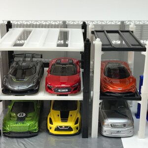 Peut inclure: Un garage &agrave; voitures &agrave; plusieurs niveaux blanc avec des poutres de soutien noires et un toit noir. Six voitures miniatures sont gar&eacute;es sur les diff&eacute;rents niveaux. Les voitures sont argent&eacute;es, rouges, orange, vertes, jaunes et argent&eacute;es.