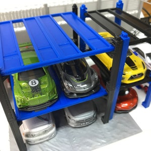 Peut inclure: Un garage &agrave; voitures miniature &agrave; plusieurs niveaux avec des supports en m&eacute;tal bleu et noir. Le garage est rempli de voitures miniatures de diff&eacute;rentes couleurs, notamment vert, jaune, noir et blanc.