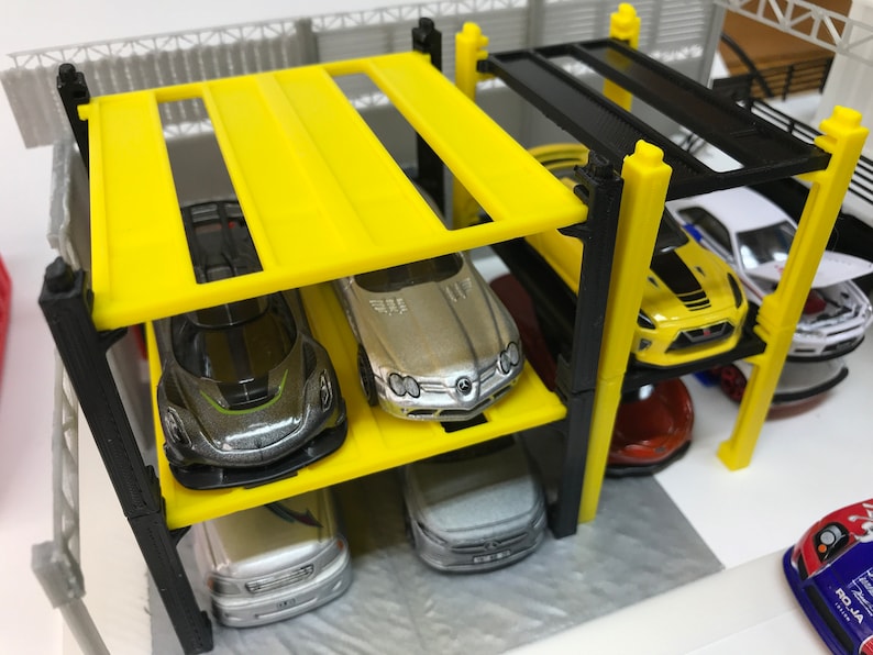 Peut inclure: Un garage &agrave; voitures &agrave; plusieurs niveaux jaune et noir avec quatre voitures miniatures gar&eacute;es &agrave; l'int&eacute;rieur. Les voitures sont une Mercedes-Benz argent&eacute;e, une voiture de sport noire et verte, une berline argent&eacute;e et une voiture de sport rouge.