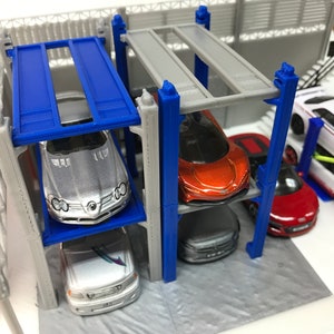 Peut inclure: Un jouet de garage &agrave; plusieurs niveaux avec quatre voitures miniatures. Le garage est en plastique gris avec des accents bleus. Les voitures sont argent&eacute;es, orange, rouge et blanche.