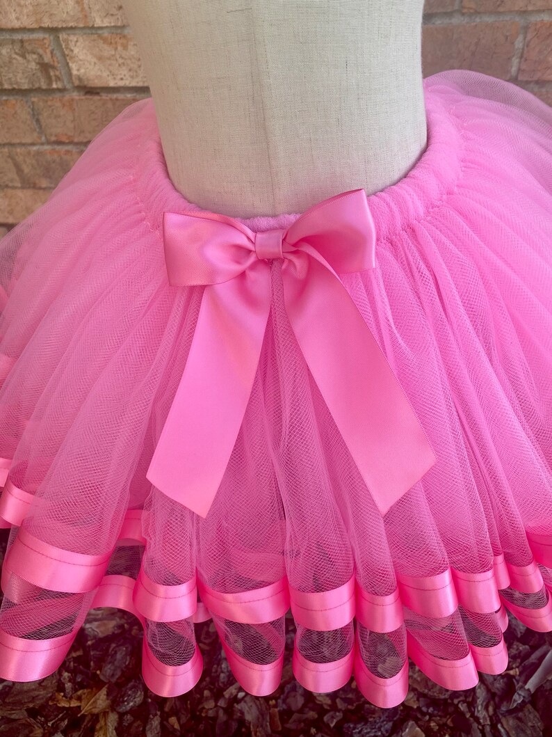 May include: Pink tulle tutu skirt with a pink satin bow and pink satin ribbon trim.