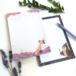 May include: Two notepad sets with whimsical illustrations. One features a fox looking up at a crescent moon against a purple and white background. The other features an owl wearing a wizard's hat and holding a wand against a dark blue and gold background.