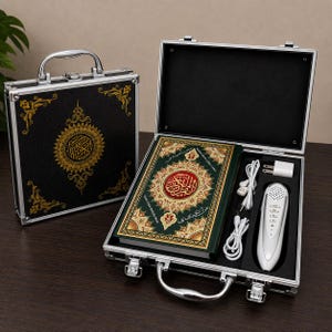 May include: A black metal carrying case with gold filigree patterns containing a green Quran with gold-embossed Arabic calligraphy, a white digital reading pen, white wired earphones, and a white power adapter, all set in a black foam insert.
