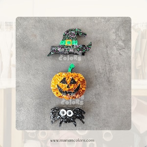 May include: Three Halloween-themed hair clips: a black witch hat with green trim, an orange pumpkin with a jack-o'-lantern face, and a black spider with googly eyes.
