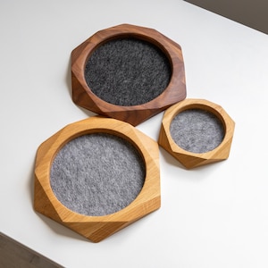 Könnte beinhalten: Drei achteckige Holzschalen mit facettierten Kanten und filzgefütterten Innenseiten. Die größte Schale besteht aus dunkelbraunem Holz mit anthrazitfarbenem Filzeinsatz, die zwei kleineren aus hellem Eichenholz mit hellgrauem Filzeinsatz.