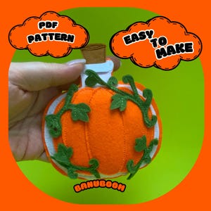 Könnte beinhalten: Eine handgefertigte orangefarbene Kürbisdekoration aus Filz mit grünen Ranken und Blättern. Der Kürbis hat einen weißen Rand und einen Korken. Der Text im Bild lautet "PDF PATTERN" und "EASY TO MAKE". Das Wort "BANUBOOM" ist ebenfalls sichtbar.