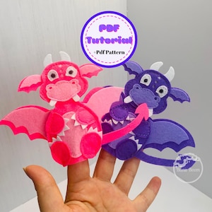 以下が含まれることがあります： ドラゴン型のフェルト製指人形が2つ。ピンクのドラゴンは白い歯と目。紫のドラゴンは白い歯と目。人形は手に乗っています。