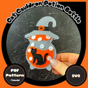 May include: A felt Halloween decoration in the shape of a cauldron potion bottle. The bottle is gray with white polka dots and an orange potion. A black cat silhouette is inside the potion. The text "Cat Cauldron Potion Bottle" is arched above the bottle.