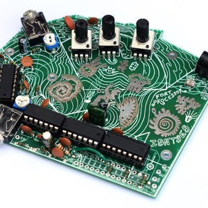 Può includere: Un circuito stampato verde con linee decorative bianche e vari componenti elettronici. La scheda ha tre manopole nere, diversi circuiti integrati neri e il testo "FORT PROCESSOR ISN'TSES".