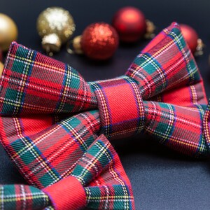 May include: A red and green plaid bow tie with a festive Christmas theme. The bow tie is surrounded by gold and red ornaments.