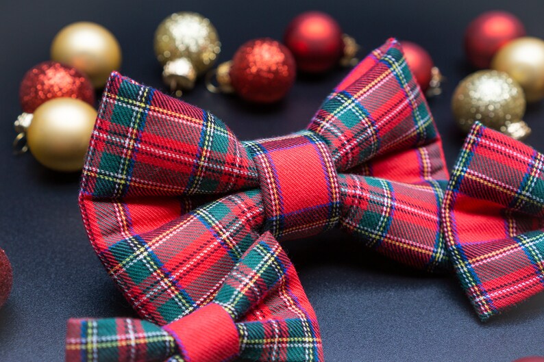 May include: A red and green plaid bow tie with a festive Christmas theme. The bow tie is surrounded by gold and red ornaments.