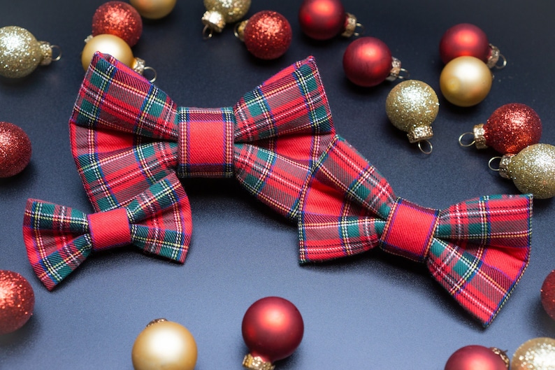 May include: Two red and green plaid bow ties with a festive Christmas ornament theme. The ornaments are red, gold, and white.