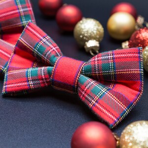 May include: A red and green plaid bow tie with a festive Christmas theme. The bow tie is surrounded by red and gold ornaments.