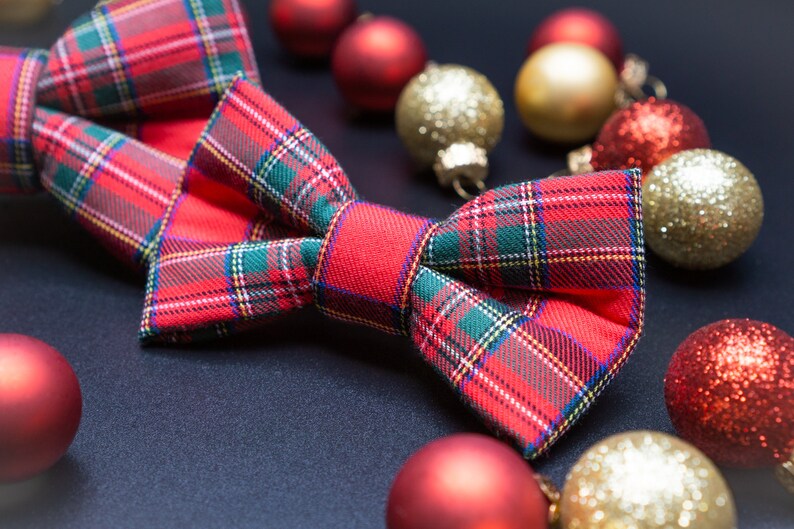 May include: A red and green plaid bow tie with a festive Christmas theme. The bow tie is surrounded by red and gold ornaments.