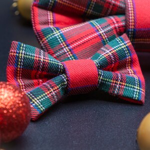 May include: A red and green plaid bow tie with a red center. The bow tie is on a black surface with red and gold ornaments.