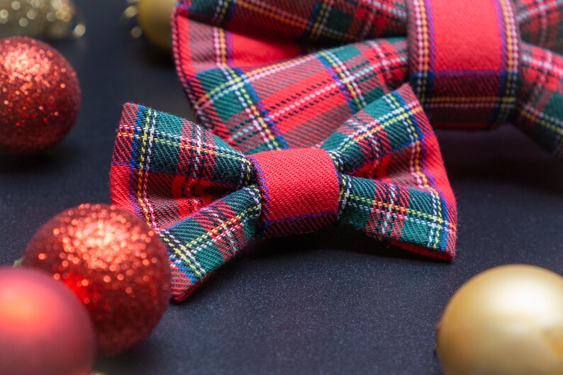 May include: A red and green plaid bow tie with a red center. The bow tie is on a black surface with red and gold ornaments.