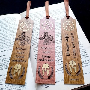 Puede incluir: Tres marcapáginas de madera con cintas marrones. Cada marcapáginas presenta un casco espartano, una ilustración de guerrero y la frase "Molon Labe, Come and take it." Un marcapáginas también dice "Leonid."