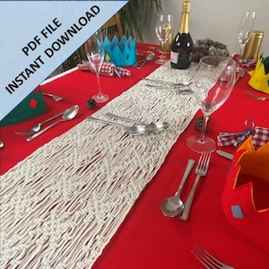 以下が含まれることがあります： 赤いテーブルクロスの上に、幾何学模様の白いマクラメテーブルランナーが置かれています。テーブルには、カトラリー、ワイングラス、そしてお祝いの飾り付けがされています。