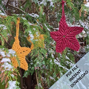 Op de afbeelding: Drie macramé ster-versieringen in rood, geel en oranje hangen aan een besneeuwde naaldbomen. De tekst "PDF FILE INSTANT DOWNLOAD" is zichtbaar in de rechter benedenhoek van de afbeelding.