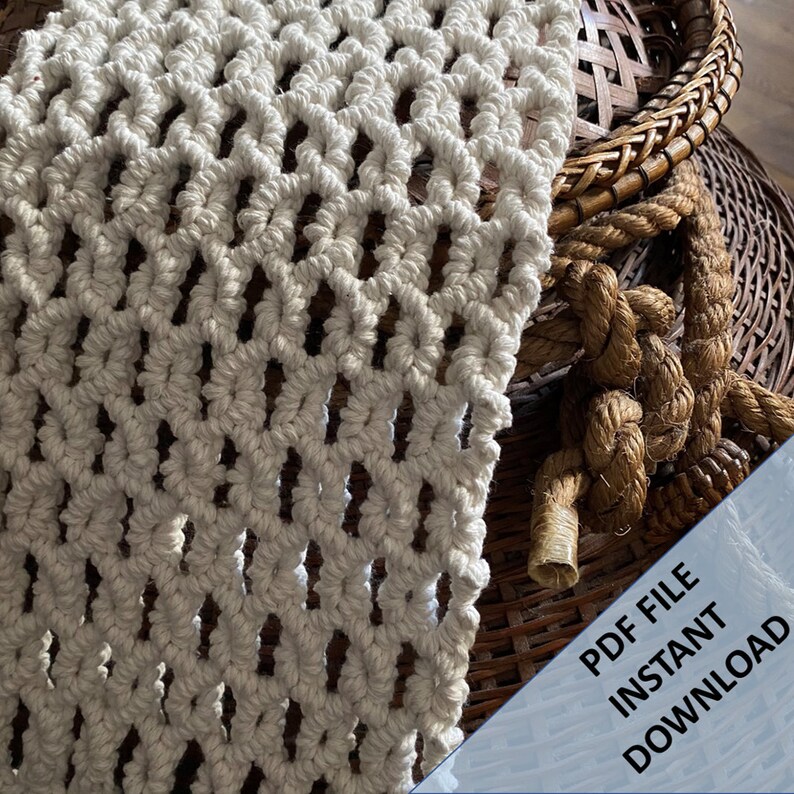 Pode incluir: Uma tape&ccedil;aria de macram&eacute; branca com um padr&atilde;o de diamante. O macram&eacute; est&aacute; pendurado sobre uma cesta tecida com uma corda.