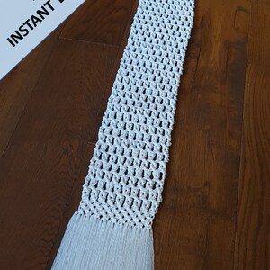 Pode incluir: Um corredor de mesa branco de croch&ecirc; com franjas em ambas as extremidades. O corredor est&aacute; colocado sobre uma superf&iacute;cie de madeira.