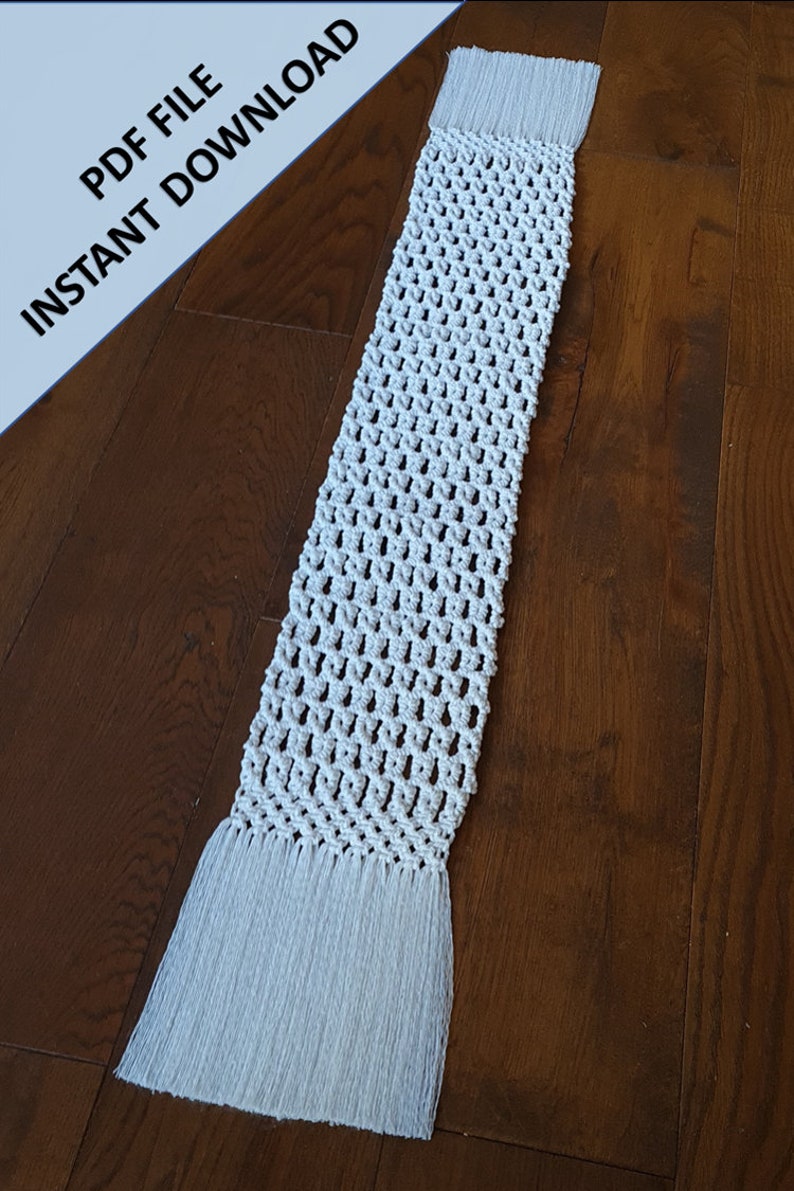 Pode incluir: Um corredor de mesa branco de croch&ecirc; com franjas em ambas as extremidades. O corredor est&aacute; colocado sobre uma superf&iacute;cie de madeira.