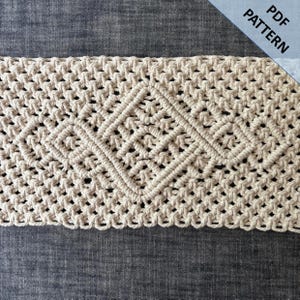 Peut inclure: Motif macramé de couleur crème avec un motif de losange central. Le macramé est fait d'un cordon épais et tissé, et le motif est visible sur un fond gris foncé. Les mots "PDF PATTERN" sont dans le coin supérieur droit.