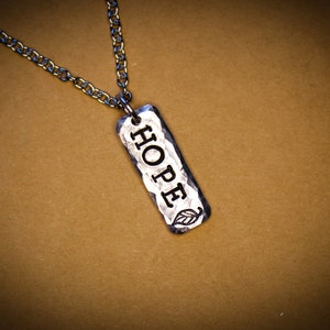 May include: A silver necklace with a hammered metal pendant that says "HOPE" with a small leaf design.