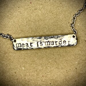 May include: A silver necklace with a hammered metal bar pendant that reads "meat is murder".